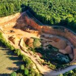 A stunning aerial shot of a large quarry contrasting sharply with lush green forests.